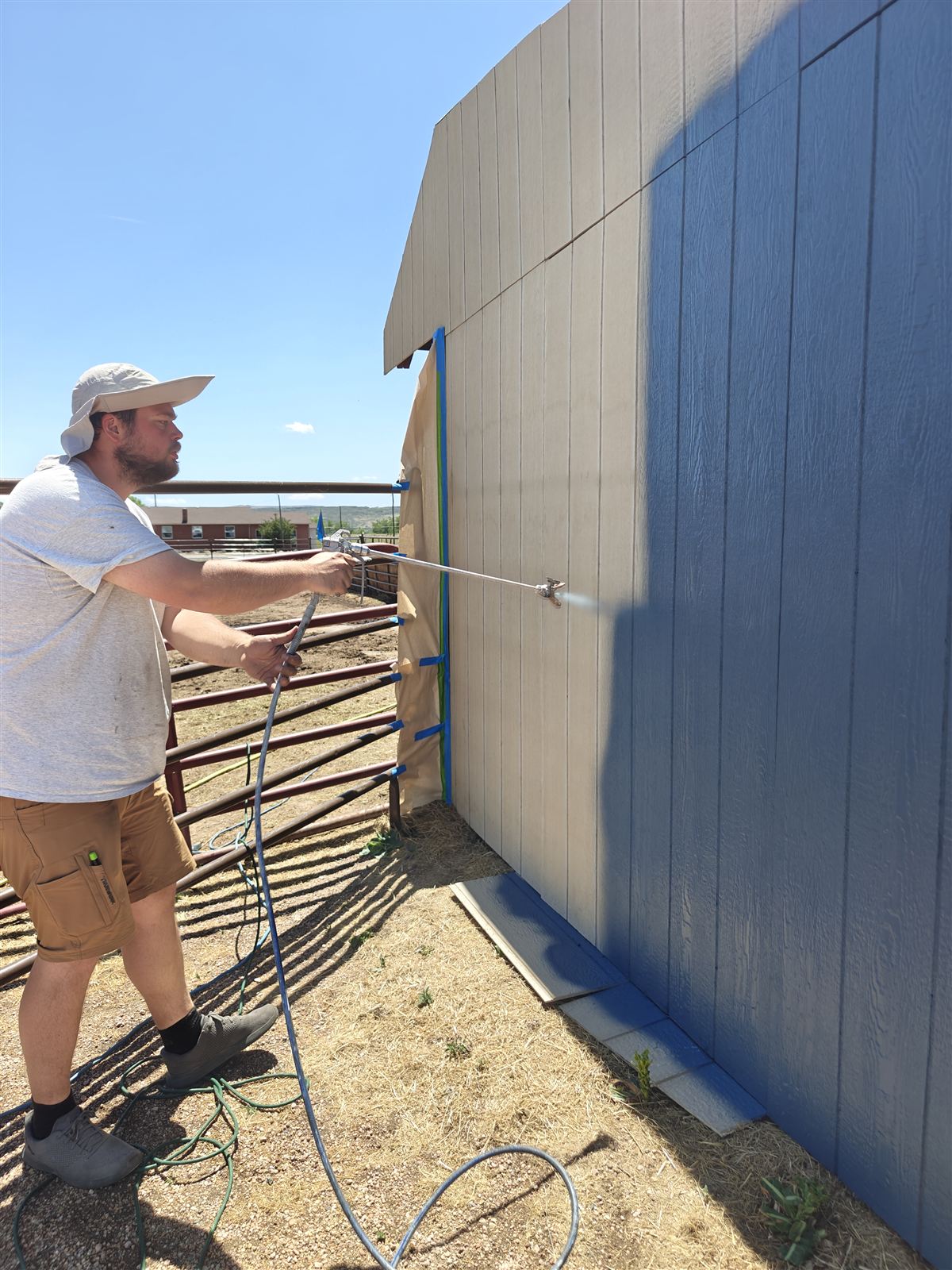 Painter spray-applying exterior paint to home siding near Golden, Colorado